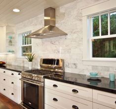 a kitchen with white cabinets and black counter tops, stainless steel hood over the stove