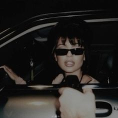 a woman in sunglasses is pointing at something on her cell phone while sitting in the back seat of a car