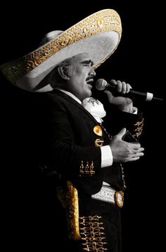 a man wearing a sombrero and singing into a microphone in front of a black background