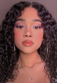 a woman with long curly hair wearing large hoop earrings and pink makeup looks at the camera