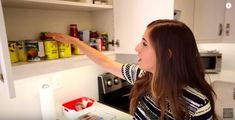 a woman is reaching for food in the kitchen cabinet and she is pointing at it