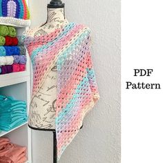 a crocheted shawl hanging on a wall next to a shelf with sweaters