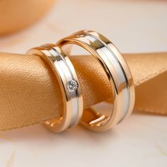 two gold wedding rings sitting on top of a yellow satin ribbon with a diamond in the center