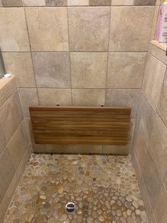 a wooden bench sitting in the middle of a stone tiled shower stall with rocks on the floor