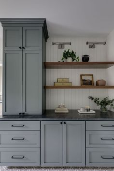 a kitchen with gray cupboards and shelves filled with pots, plants and bowls on top of them