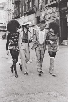 three people walking down the street with one person wearing a hat and another man in a suit