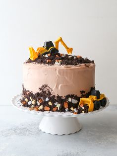 a cake with chocolate frosting and construction trucks on top is sitting on a white pedestal