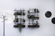 three shelves with plants and books on them against a white wall next to a lamp