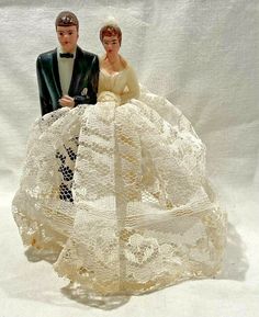 a bride and groom figurine sitting on top of a white cloth covered table