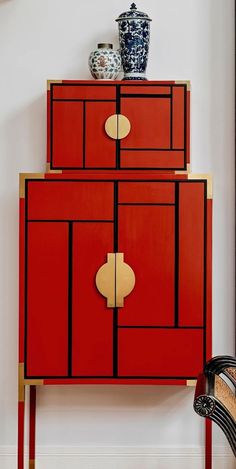 a red cabinet with gold trim and two vases on top, against a white wall