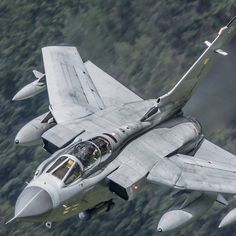 a fighter jet flying through the air with trees in the background