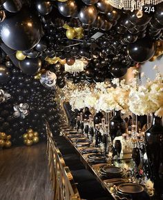 a long table with black and gold balloons hanging from it's ceiling, filled with white flowers