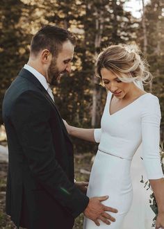 a pregnant woman standing next to a man in a suit and tie with his hand on her belly