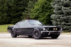 an old muscle car is parked in a parking lot with trees and bushes behind it