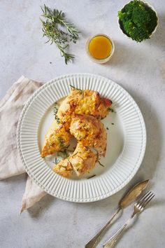 two pieces of chicken on a white plate next to broccoli and orange juice