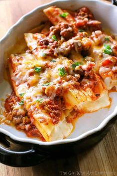 a white dish filled with lasagna shells covered in meat and cheese on top of a wooden table