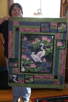 a woman holding up a large quilt with swans on the water and lily padding