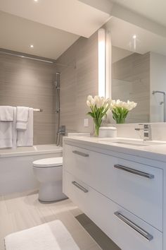 a white bathroom with flowers and towels on the counter next to the bathtub, toilet and shower