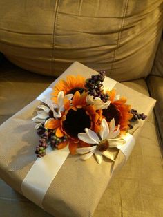 a gift wrapped in white paper with sunflowers and other flowers on the side