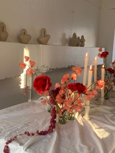 flowers and candles sit on a table in front of white vases with red roses