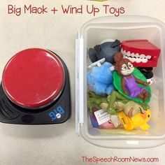 a plastic container filled with lots of toys next to a red button on top of a white table