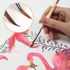 a hand holding a paintbrush and drawing flamingos