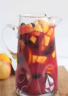 a pitcher filled with fruit sitting on top of a wooden table