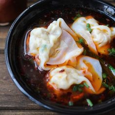 some dumplings are in a black bowl on a wooden table