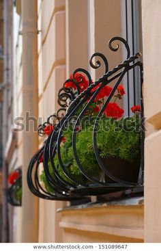 an iron planter with red flowers hanging from the side of a building in europe