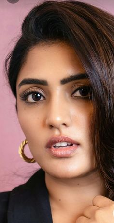 a close up of a person wearing gold hoop earrings and a black jacket with pink background