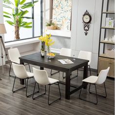 a dining room table with white chairs and a clock on the wall in front of it