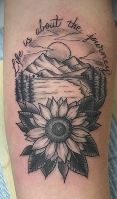 a sunflower tattoo on the arm with mountains in the background and words above it