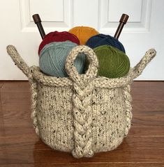 a basket with yarn and knitting needles in it on the floor next to a door