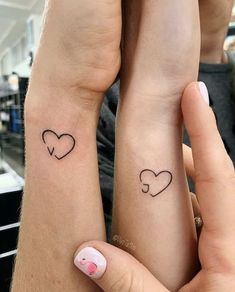 two people with matching tattoos on their arms holding each other's hands and looking at the camera