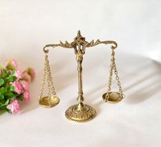 a golden scale with two gold scales on it and some pink flowers in the background