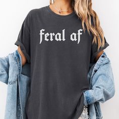 This Comfort Colors Feral AF Unisex T-Shirt is packed with attitude in minimalistic way!  Whether you're treating yourself, or gifting it to someone you love, this will quickly become your go-to tshirt! **Please size up if you are looking for the oversized t-shirt look! This is a unisex fit and runs true to size. For a better idea, please refer to the size chart in the pictures.** - Made 100% with ring-spun cotton. The soft-washed, garment-dyed fabric brings extra coziness to your wardrobe while Edgy Cotton Slogan Tops, Cotton Grunge Slogan Tops, Grunge Cotton Slogan Tops, Edgy Cotton Tops With Text Print, Band Merch Cotton Tops With Funny Text, Cotton Band Merch Top With Funny Text, Grunge Slogan Top With Relaxed Fit, Grunge Style Slogan Top With Relaxed Fit, Grunge Cotton Shirt With Letter Print