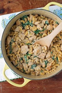 a pot filled with pasta and meat on top of a wooden table next to a spoon