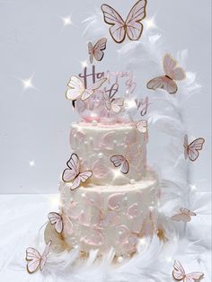 a three tiered cake with pink frosting and butterflies on top, surrounded by white feathers