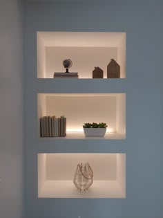 three white shelves with books and vases on them in a blue walled wall area