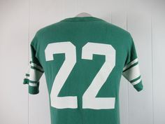 "Vintage 1970s or 80s college t shirt. Made of green cotton with thick white college graphics: Michigan State #22. Has Champion blue block label. Size large. Actual measurements are: 39\" around the chest 39\" around the waist 20\" shoulder seam to shoulder seam 28\" overall length In very good condition with 3\" of seam repair to the cuff." Green T-shirt For College Football Season, Green Varsity Crew Neck T-shirt, Green Varsity T-shirt With Letter Print, Retro Green T-shirt For Sports, Vintage Graphic Print Football T-shirt, Vintage Graphic T-shirt For Football Season, Vintage Graphic Print T-shirt For Football Season, Vintage Style Screen Print Fan Gear T-shirt, Vintage Screen Print T-shirt For Fans