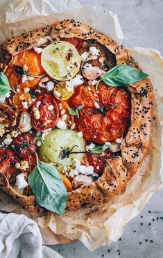 a pizza topped with tomatoes, cheese and basil on top of a piece of wax paper