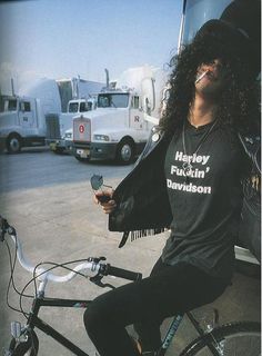 a man sitting on top of a bike in front of a semi - truck with long hair