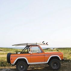 an orange and white truck with a surfboard on the roof parked in a field