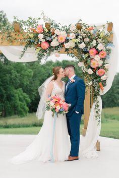 a bride and groom kissing under an arch with flowers