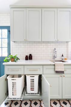 a kitchen with white cabinets and two baskets under the sink in front of the counter