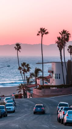 cars are parked on the side of the road near the ocean and palm trees at sunset