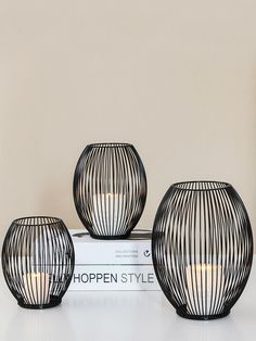 three black vases sitting next to each other on top of a white bookcase