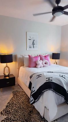 a white bed with pink and black pillows in a bedroom next to two nightstands