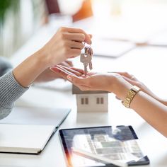 two people exchanging keys to each other in front of a house model on a table