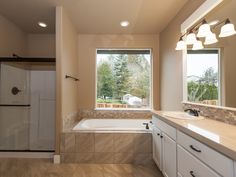 a bathroom with a tub, sink and large window overlooking the trees outside in the day time